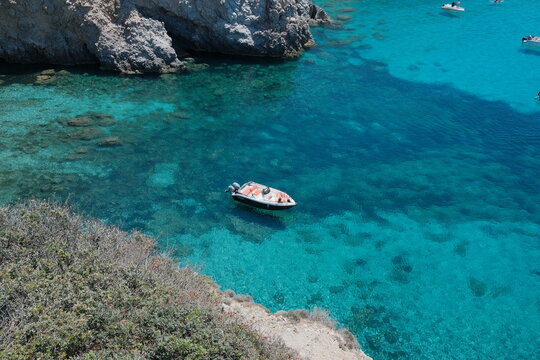 Panoramic view of a secluded turquoise bay surrounded by rugged limestone cliffs and crystal-clear Mediterranean water beneath a cloudless summer sky at Tsigrado Beach, Milos, Greece.