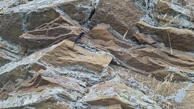 Layered rock formation with sedimentary stone strata. Natural geological structure showing crustal movement in a rough cliff surface. Ancient mountain texture.
