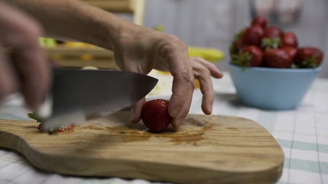 Small, beautiful strawberry being sliced on cutting board with knife - closeup, slow motion shot