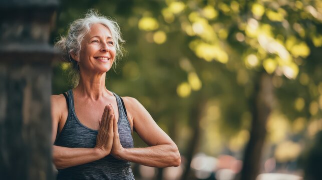 Smiling mature woman with hands clasped in prayer pose outdoors during a serene morning yoga session