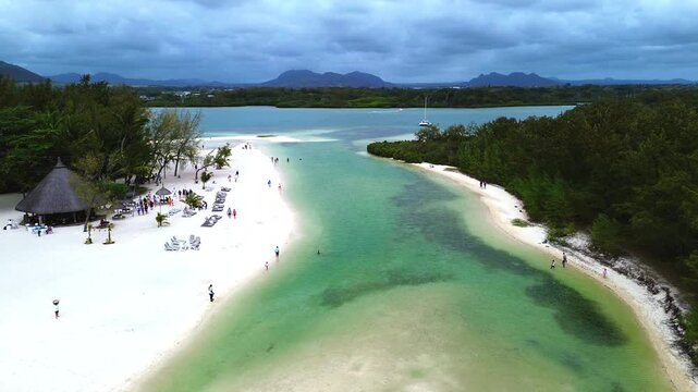Aerial view capturing the iconic coastal layout of Ile aux Cerfs (Deer Island), Mauritius. Winding turquoise lagoon channel with clear shallow water, bordered by an expansive white sand beach featurin