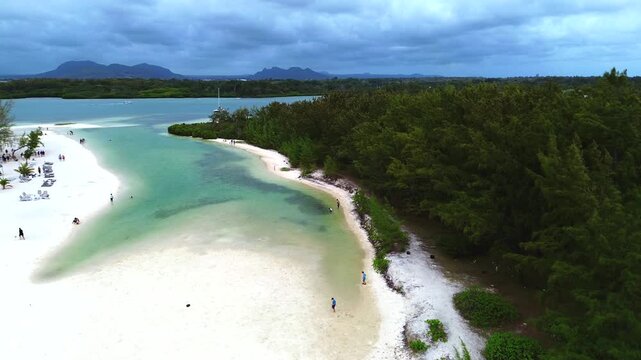 Aerial view capturing the iconic coastal layout of Ile aux Cerfs (Deer Island), Mauritius. Winding turquoise lagoon channel with clear shallow water, bordered by an expansive white sand beach featurin