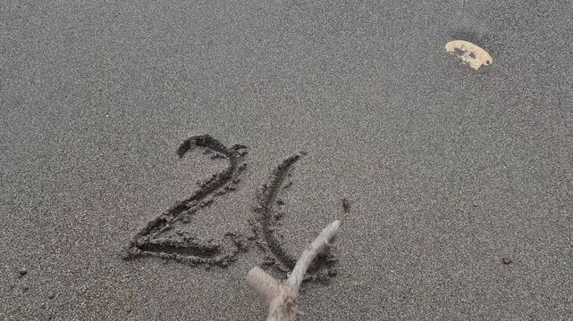 2027 year date written by a hand with a stick on the beach sand. High-angle static shot.