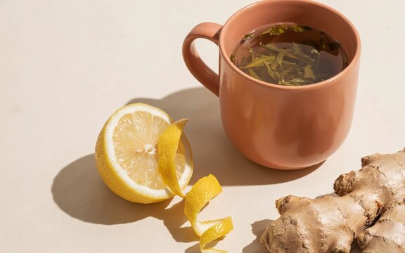 Peach-colored mug of herbal tea with fresh lemon slice and ginger root