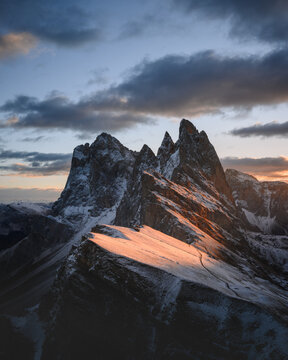 Warm sunrise light illuminates the snow-covered peaks of Seceda in the Dolomites. Dramatic alpine landscape with rugged limestone formations and fresh snowfall
