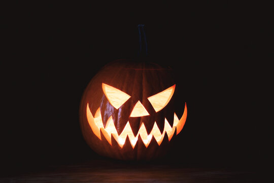 Spooky jack o lantern illuminated from within on a dark background with dramatic lighting. Traditional Halloween pumpkin carving with evil expression and glowing teeth