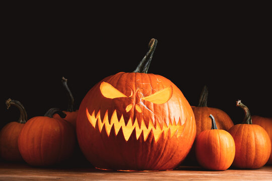 Glowing carved pumpkin lantern surrounded by pumpkins creating a festive Halloween display. Warm candlelight and dramatic shadows enhance the spooky holiday atmosphere