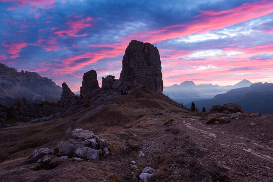Cinque Torri beneath colorful sunrise clouds in the Dolomites during early autumn. Iconic limestone towers rising above rugged alpine terrain in the Italian Alps