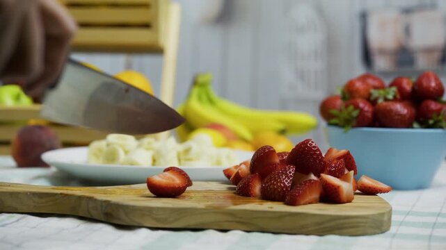 Chef's hands holding sharp knife and slicing up strawberries on cutting board - closeup tracking shot