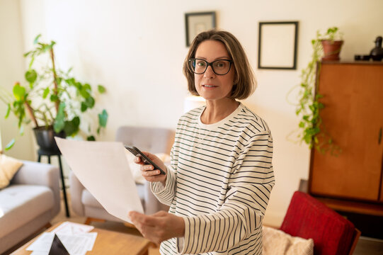 Middle aged woman standing with paper and smartphone