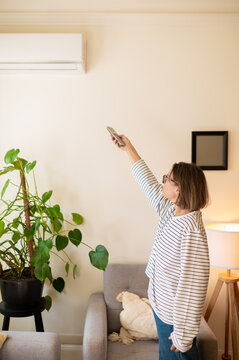 Middle aged woman using air conditioner remote control
