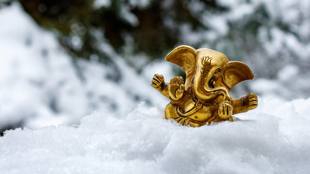 Golden Ganesha figurine resting on fresh snow with winter forest background and copy space