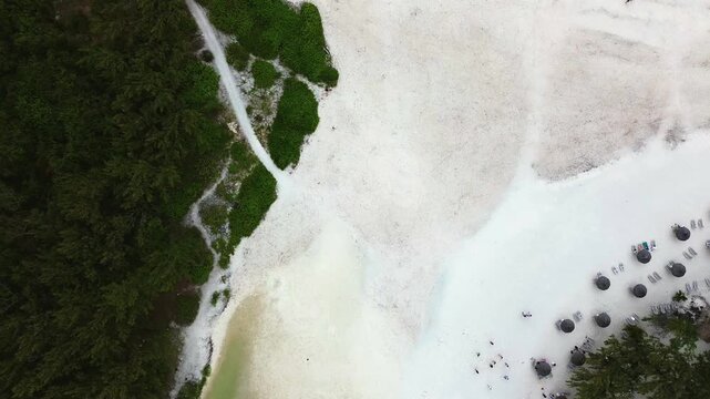 Aerial drone shot capturing a bird's-eye perspective of a rugged coastline in Mauritius. The right side features a patch of pristine white sand beach covered in fractured, dark black volcanic lava roc
