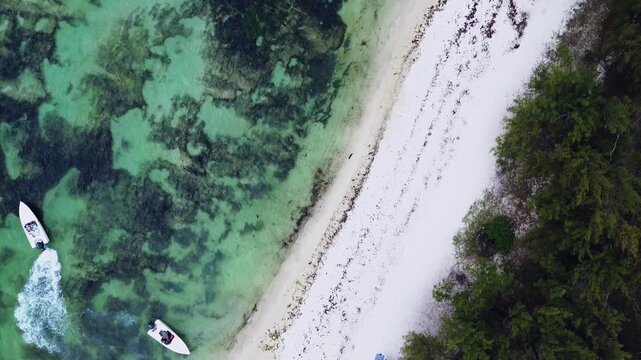 Aerial drone shot capturing a bird's-eye perspective of a rugged coastline in Mauritius. The right side features a patch of pristine white sand beach covered in fractured, dark black volcanic lava roc