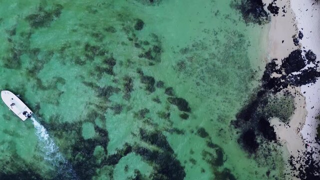 Aerial drone shot capturing a bird's-eye perspective of a rugged coastline in Mauritius. The right side features a patch of pristine white sand beach covered in fractured, dark black volcanic lava roc