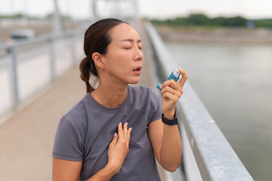 Asian woman using inhaler for asthma attack outdoors