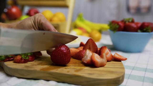 Sharp knife cutting up strawberry on cutting board - slow motion closeup shot