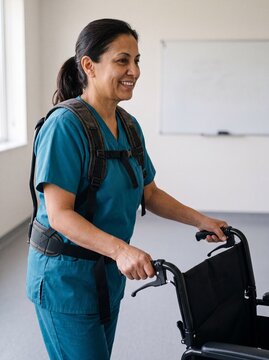 Nahaufnahme einer l&auml;chelnden Pflegekraft mit Exoskelett die einen leeren Rollstuhl schiebt im hellen Therapieraum