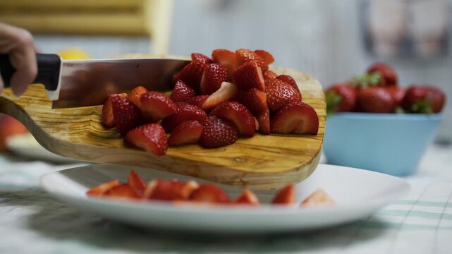 Closeup shot of knife being used to move sliced strawberries onto plate