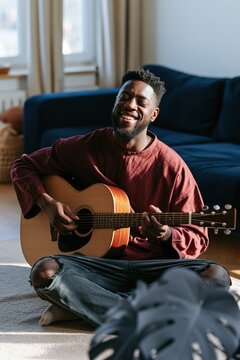 Young man playing acoustic guitar in bright living room for upbeat music background and lifestyle banner design