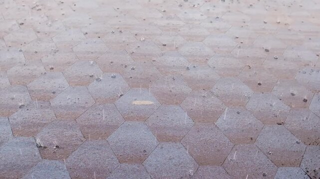 Rainwater cascades over hexagonal pavement tiles, illustrating the dynamic movement of droplets across the surface in a natural environment