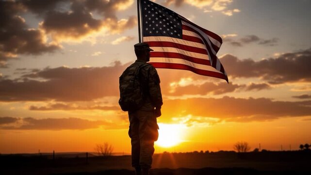 Silhouette of a soldier standing before an american flag at sunset