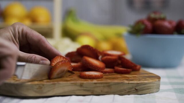 Chef using small knife to slice up strawberry on cutting board - closeup, tracking shot