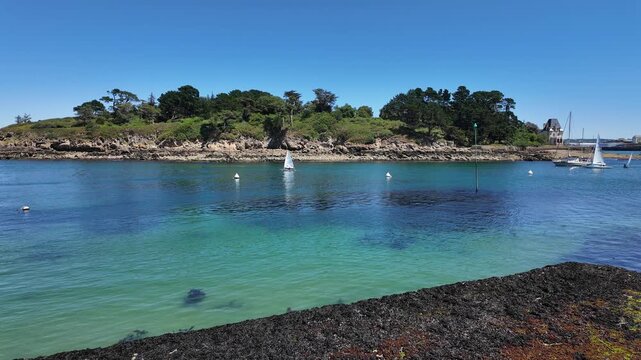 DOUARNENEZ, FRANCE &ndash; July 4, 2026: Slow right-to-left pan across a turquoise bay with anchored sailboats in Douarnenez, Brittany, France. Calm summer harbor scene on the Atlantic coast with clear blue