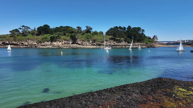 DOUARNENEZ, FRANCE &ndash; July 4, 2026: Slow right-to-left pan across a turquoise harbor with anchored sailboats and a rocky shoreline in Douarnenez, Brittany, France. Sunny summer day on the Atlantic coas