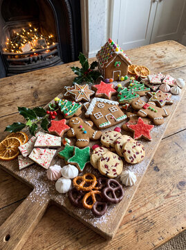 A wooden cutting board beautifully arranged with delicious gingerbread cookies star biscuits dried orange slices and pretzels near a fireplace.