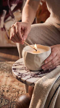 Person lighting match to ignite luxury ceramic soy wax candle on marble table