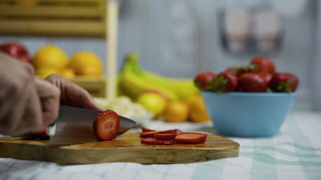 Person taking strawberries from bowl and slicing them up on cutting board - closeup