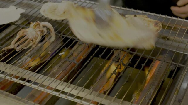 A scene of squid and scallops being grilled and flipped over at a market in Hokkaido.