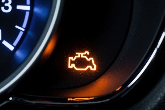 Orange check engine light glows on vehicle dashboard console. Car malfunction indicator symbol signals urgent repair need for automobile motor system. Close up view of modern transport tachometer