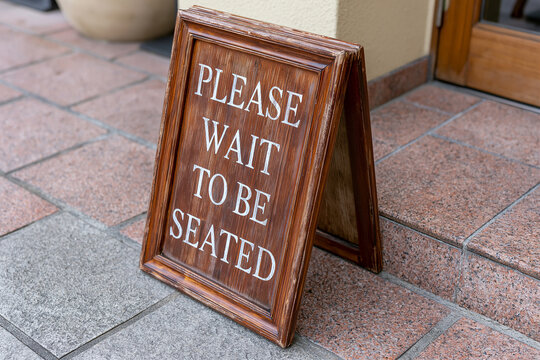 PLEASE WAIT TO BE SEATED wooden A-frame sign at an entrance