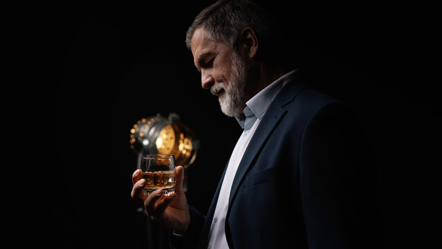 Handsome businessman in stylish suit holding glass whiskey on dark