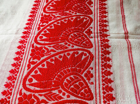 Close-up of a traditional Assamese Gamosa fabric texture featuring iconic red and white woven patterns.