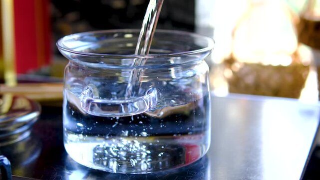 Fresh clean water poured into clear glass pot before cooking on kitchen stove creating simple homemade meal preparation close up food video