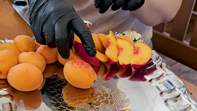 Apricot and nectarine wedges arranged on shiny silver serving tray by chef in black gloves for elegant fruit presentation, close up
