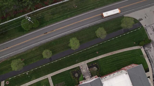 Overhead drone aerial view of school bus transportation taking students to nearby suburban education center in central Ohio from above as yellow and white long vehicle coach shuttle pulls into lot 4k