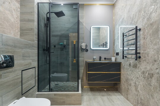A bathroom features a glass shower, a modern sink, and a mirror. The walls are made of stone, and there are metal details. It is well-lit and organized