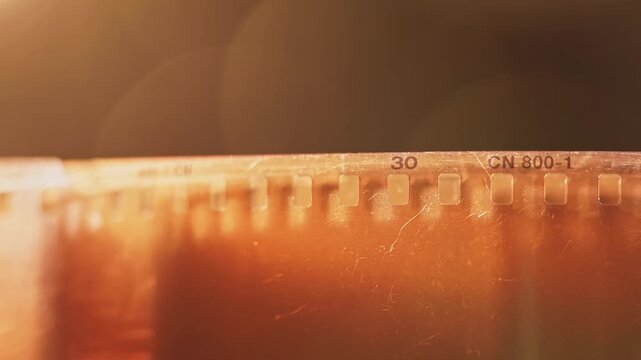 Slow motion close up texture and damaged view of warm 35mm film reel with no shots, broken scratched elements, and badly exposed dirty strip from cinematography photographic spool tool in slow mo 4k