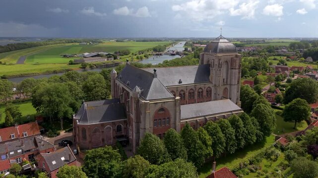 Beautiful high altitude aerial panoramic perspective of historic medieval Grote Kerk church cathedral village red roof houses canal lock dramatic sky and countryside in sunlight