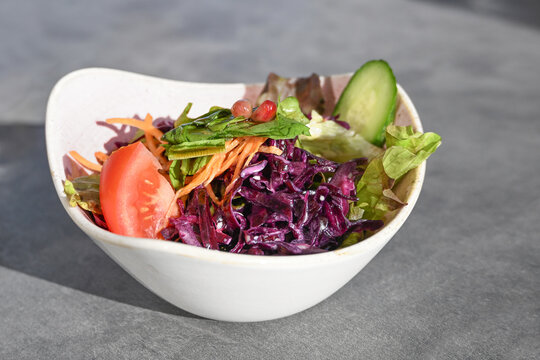 Fresh summer salad with a light dressing in a bowl, made with vegetables like red cabbage, carrots, lettuce, cucumbers, and tomatoes, copy space, selected focus