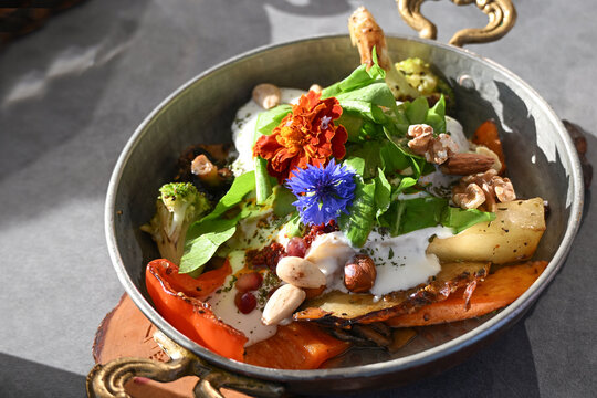 Sauteed vegetables with garlic yogurt sauce, lettuce, nuts, and garnish from colorful flowers, served in a copper casserole dish, meal in Turkish style, selected focus
