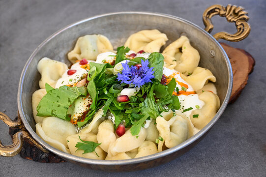 Manti, Turkish dish consisting of stuffed dumplings, served with garlic yogurt sauce and a lettuce salad, garnished with a blue cornflower blossom in a decorated metal pan