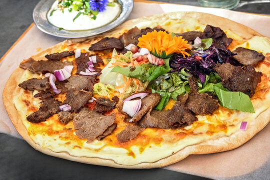Tarte flambee topped with doner kebab meat, onions, salad, and colorful flowers, a creative take on the traditional dish, selected focus, narrow depth of field