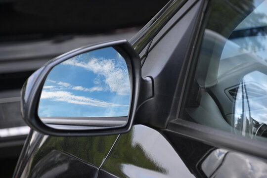 Rearview mirror of a black car reflecting a blue sky with clouds, symbol of the memory or longing to drive far away on an adventure, travel, traffic and transport concept, copy space
