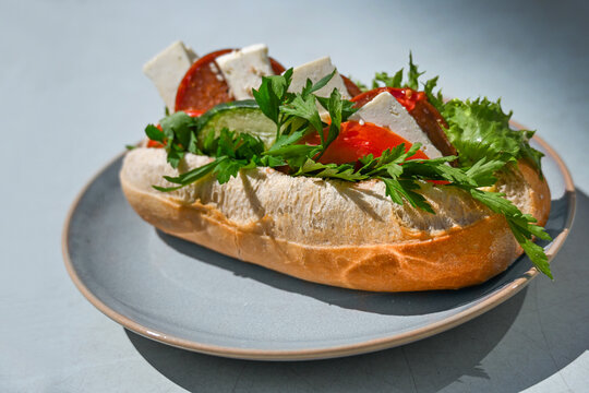 Crispy bread roll filled with Sucuk, a Turkish sausage, also parsley, lettuce, tomatoes, cucumbers, and feta cheese, served on a gray blue plate, copy space
