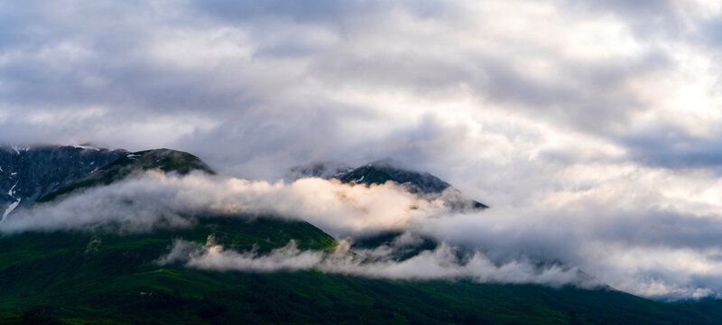First rays of morning sun light rain clouds and mountain tops along Alsek River